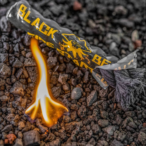 Captain's Loot Kit fire starter, a black tube with yellow Black Beard logo, igniting on dark rocks