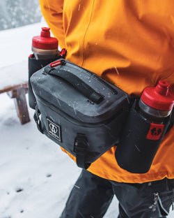 Hydration-ready Uncharted Park Pack waist pack worn in the snow by a person in an orange jacket