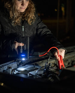 Jump starter in use, a woman connects Uncharted Zeus Pro to a car battery at night