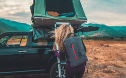Overlanding rooftop tent on a truck with a woman climbing a ladder, carrying an Uncharted seventy2 shell