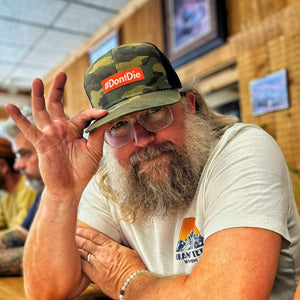 Hero Hat: bearded man wearing camouflage trucker hat with orange #DontDie patch