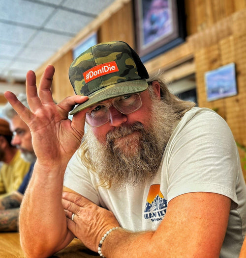 Hero Hat: bearded man wearing camouflage trucker hat with orange #DontDie patch