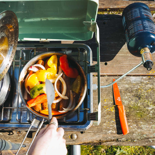 Ignik Outdoors TapRack Refillable Propane System connected to a portable camping stove cooking peppers and sausage