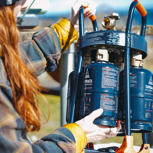 Ignik TapRack Refillable Propane System with person loading blue cylinders, great for camping