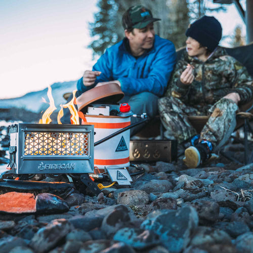 Ignik FireCan Deluxe portable propane fire pit with two people enjoying a fire on rocky riverbank