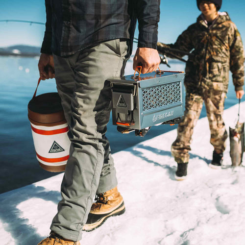 Ignik FireCan Deluxe Fire Pit and cooler carried by a person on a snowy lake for ice fishing