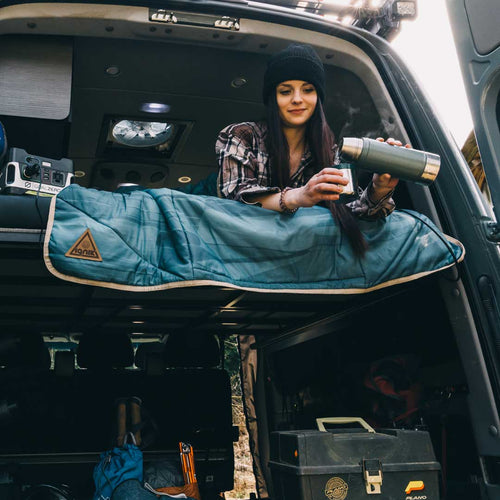 Topside Heated Blanket by Ignik Outdoors on a camper bed with a woman pouring steaming coffee