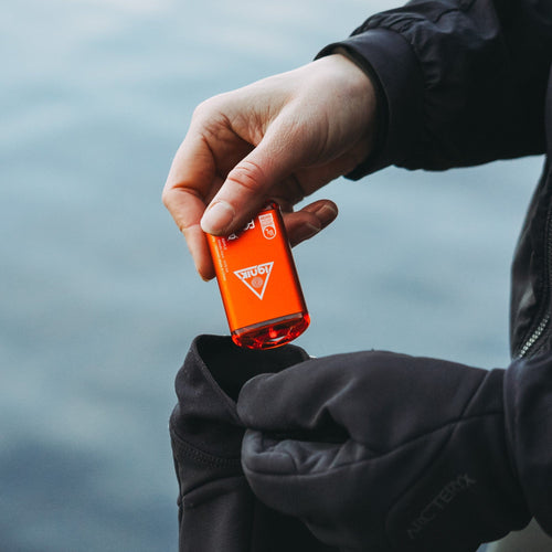 Ripple Rechargeable Hand Warmer by Ignik, bright orange, being put into a black glove outdoors for warmth