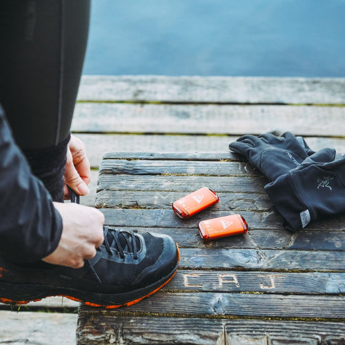 Ignik Outdoors Ripple Rechargeable Hand Warmers on wooden dock with person tying shoe, next to Arc'teryx gloves