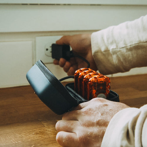 Ignik Ripple Rechargeable Hand Warmers in open case, person plugs charger into wall outlet