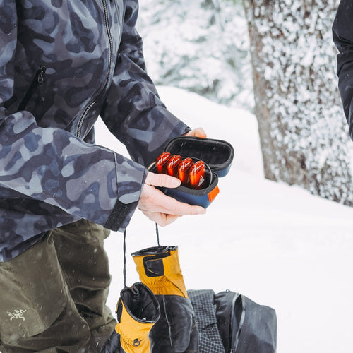 Ignik Ripple Rechargeable Hand Warmers in a compact case, held in a snowy outdoor setting