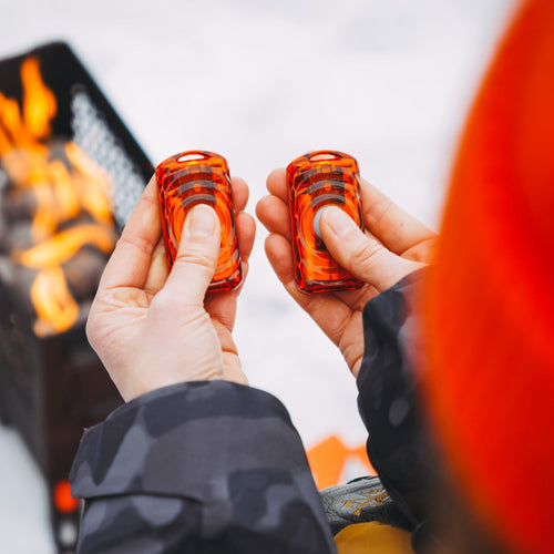 Ignik Ripple Rechargeable Hand Warmers held in hands against an outdoor fire pit background