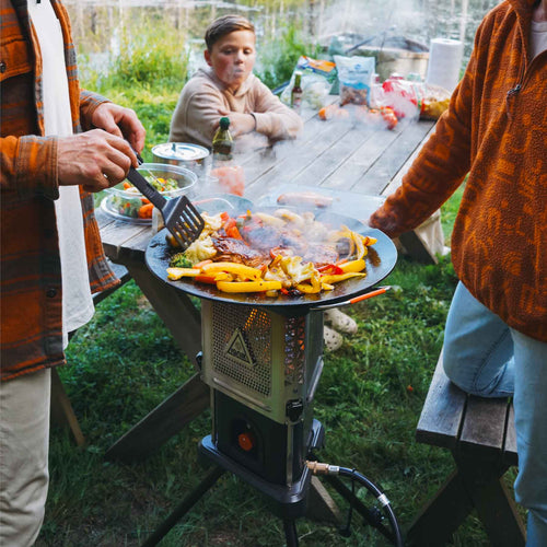 Ignik Skullet Deluxe Heater Stove Cook Set cooking meat and vegetables on an outdoor griddle for a family meal