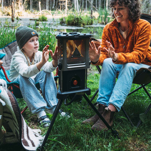 Ignik Outdoors Skullet Deluxe Heater Stove Cook Set, a portable camping heater, warming two campers by a pond