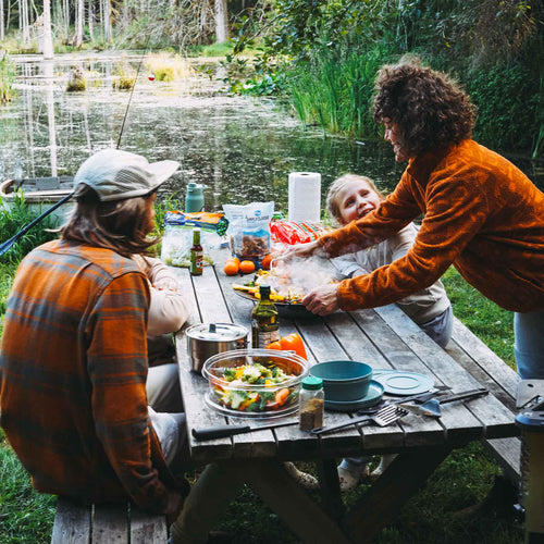 Ignik Skullet Deluxe Heater Stove Cook Set in use, family enjoying steaming meal at a lakeside picnic table
