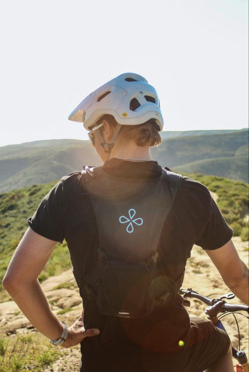 Puribag Adventure Pack black water filter pack with glowing logo worn by a biker on a mountain trail