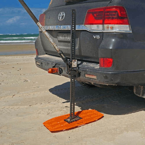 MAXTRAX JaxBase orange recovery board supporting a Hi-Lift jack to lift a vehicle from beach sand