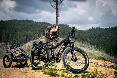 Mule Bakcou electric fat-tire hunting bike with gear trailer on a dirt trail, hunter scouting