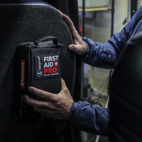 Person holding a first aid kit labeled 'First Aid Pro' in a vehicle.