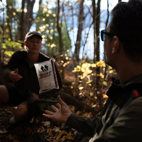 Two people in a forest setting with one throwing a triage kit
