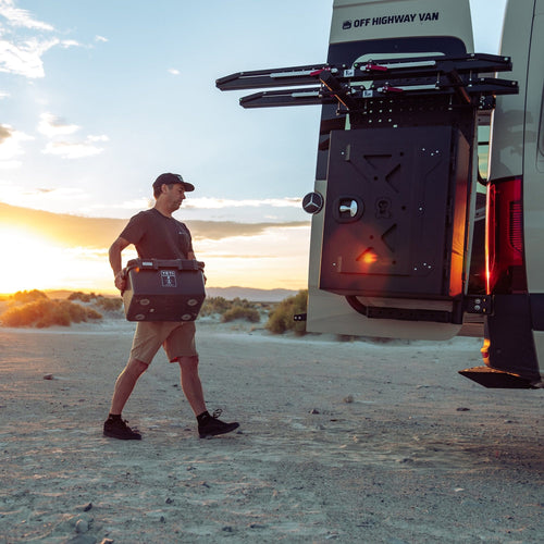 Man walking with a basecamp 30L towards an off-road vehicle with a sunset in the background