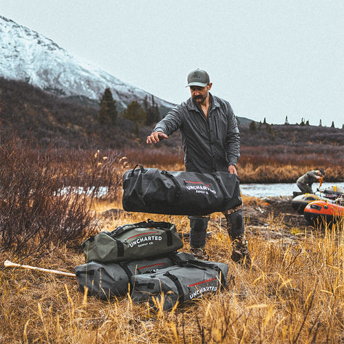 A man stacking Uncharted Vault duffels in a wilderness setting.
