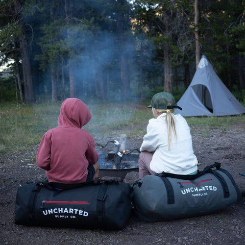 2 kids setting on 65L vaults roasting marshmallows over a campfire