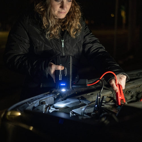 Person using a zeus pro jump starter to jump a car battery at night.