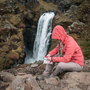 Person in a pink jacket sitting on rocks using a triage kit with a waterfall in the background
