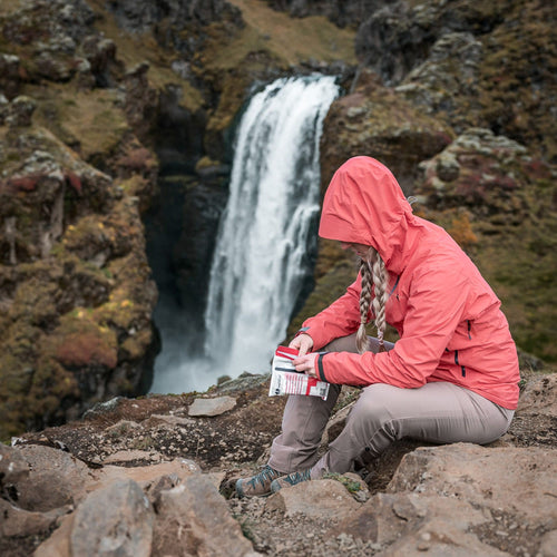 Person in a pink jacket sitting on rocks using a triage kit with a waterfall in the background