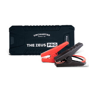 A portable jump starter named 'THE ZEUS PRO' by Uncharted Supply Co., featuring a black case and red jumper cables.