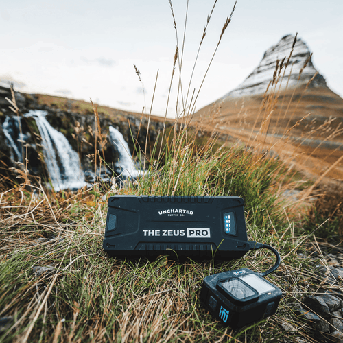 Uncharted Zeus Pro jump starter in a natural setting with mountains and waterfalls.