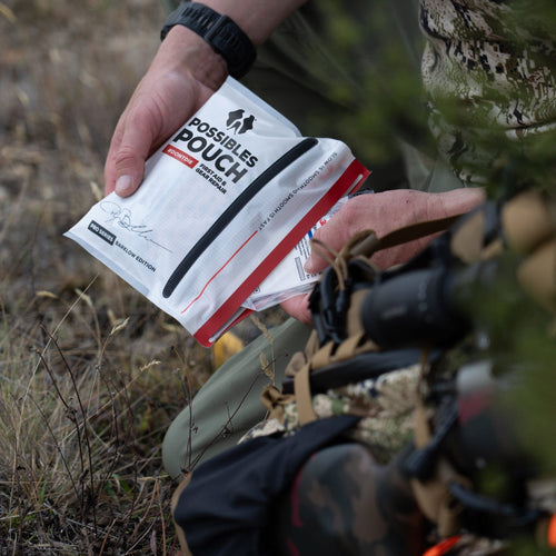 Person holding a 'Possibles Pouch' in a natural setting with binoculars and camouflage gear.