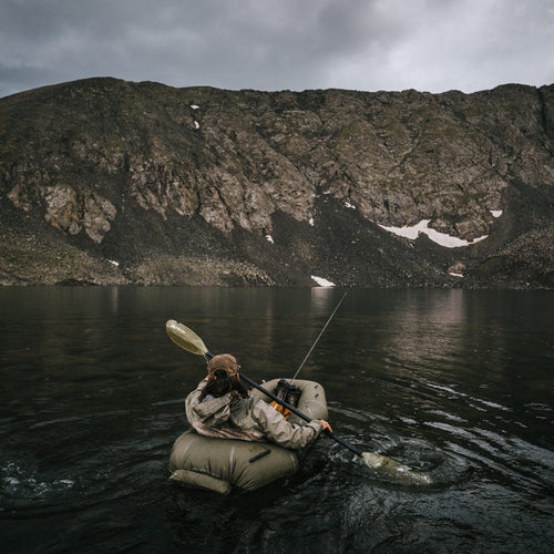 Person in a rapid raft on a lake with a mountainous background