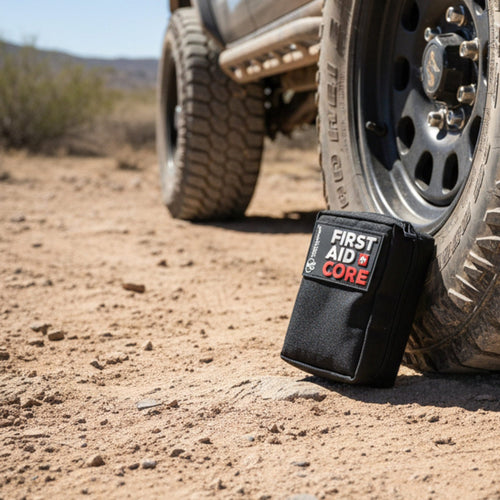 First Aid Core tactical pouch on sandy ground next to an off-road vehicle tire, ideal for an emergency medical kit