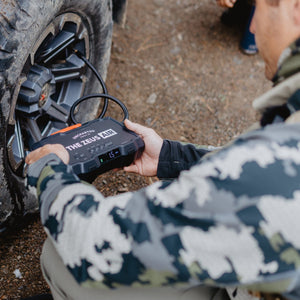 Person using a zeus air tire inflator next to a vehicle tire outdoors