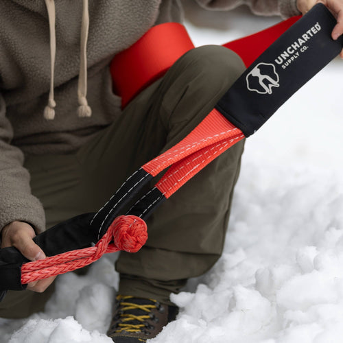 The Overlander vehicle recovery soft shackle, red, held by a person in snow, Uncharted Supply Co.