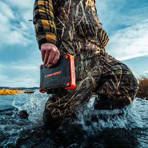 Poseidon XL: Dark Energy's rugged power bank held by a person wading through splashing water