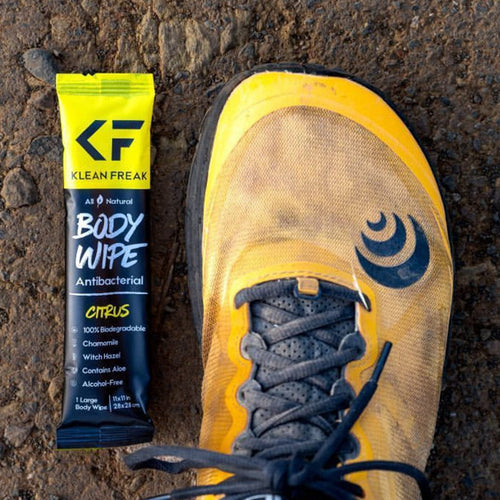 Body Wipes, Klean Freak individual antibacterial wipe next to a yellow trail running shoe on a dirt path for outdoor refresh