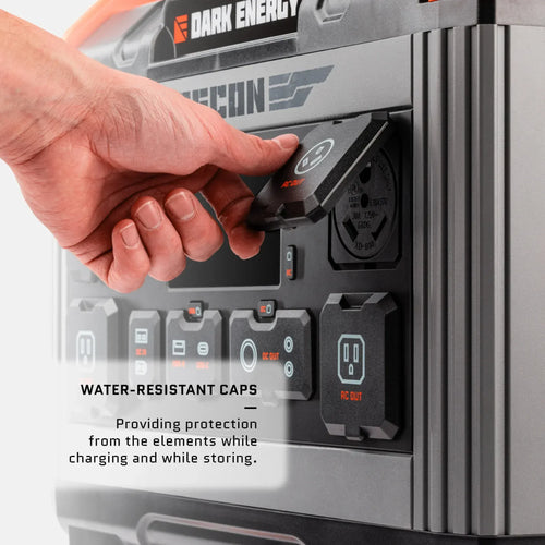Dark Energy Recon 2000 portable power station. Hand lifts a water-resistant cap protecting an AC outlet