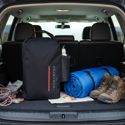 Seventy2 Core black waterproof survival kit backpack with water bottle, hiking boots, and sleeping bag in car trunk