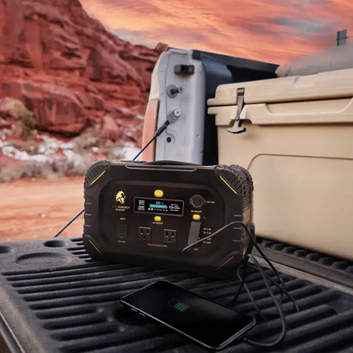 Lion Summit black & yellow portable power station charging phone on truck tailgate, with red rock desert sunset