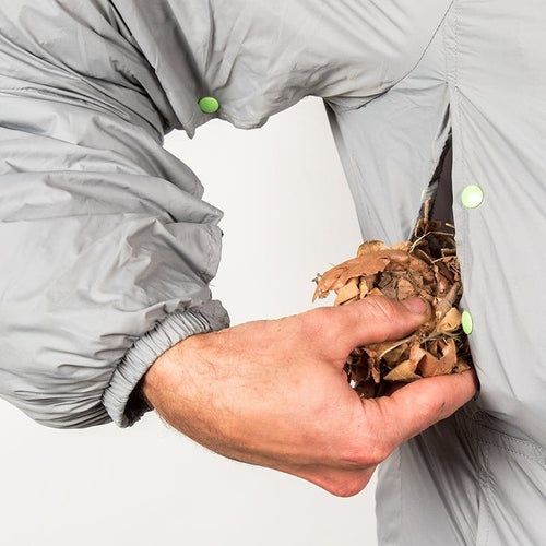 The Hideaway Weather-Resistant Windbreaker, gray, hand adding dry leaves for insulation into a survival jacket pocket