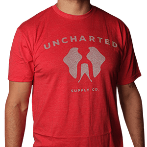 Red Uncharted Supply Co. Logo T-shirt worn by model, featuring white 'Uncharted' text & stylized wing graphic