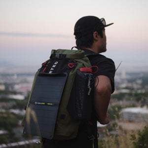 Goal Zero Nomad 10 Solar Panel, a portable solar charger, attached to a person's backpack overlooking a city